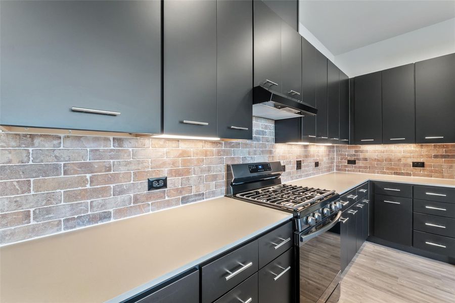 Kitchen featuring black range with gas stovetop, under cabinet range hood, dark cabinets, light countertops, and light wood-style flooring