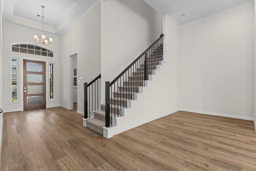 Impressive entryway with soaring ceilings, wood-look large plank tile flooring, and views of the sweeping iron  staircase.