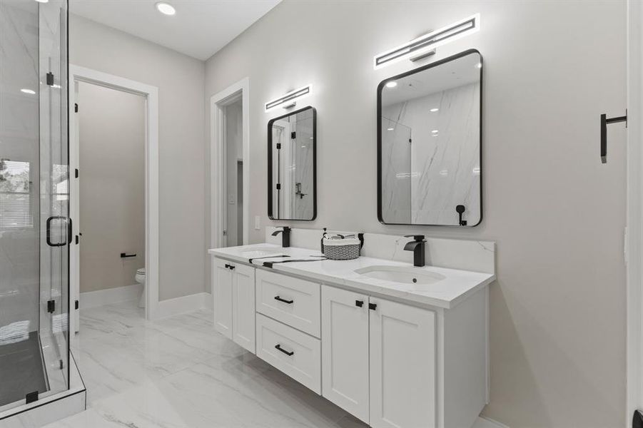 Bathroom featuring a marble finish shower, double vanity, and light marble finish floors
