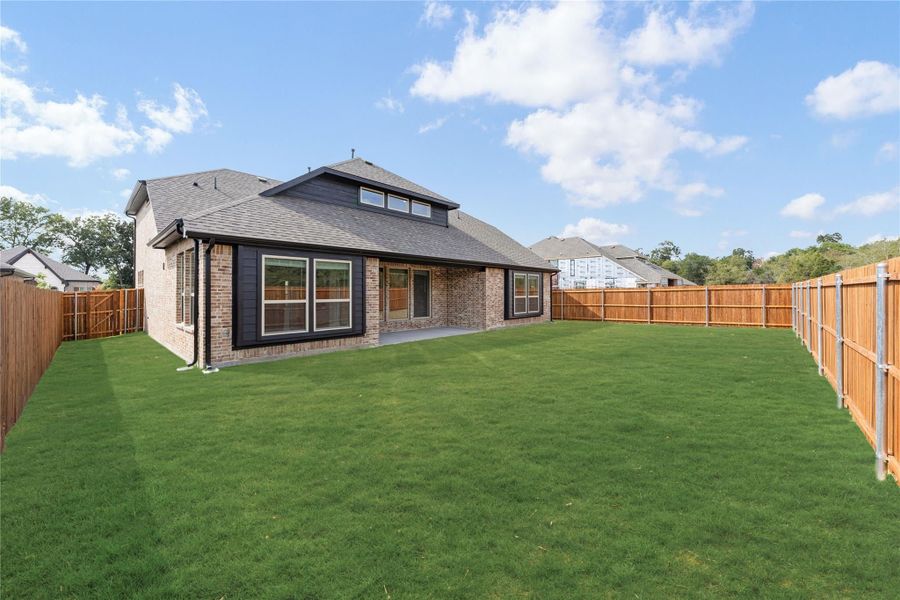 Backyard of brick home with large green lawn, wood privacy fence, and covered patio with large windows