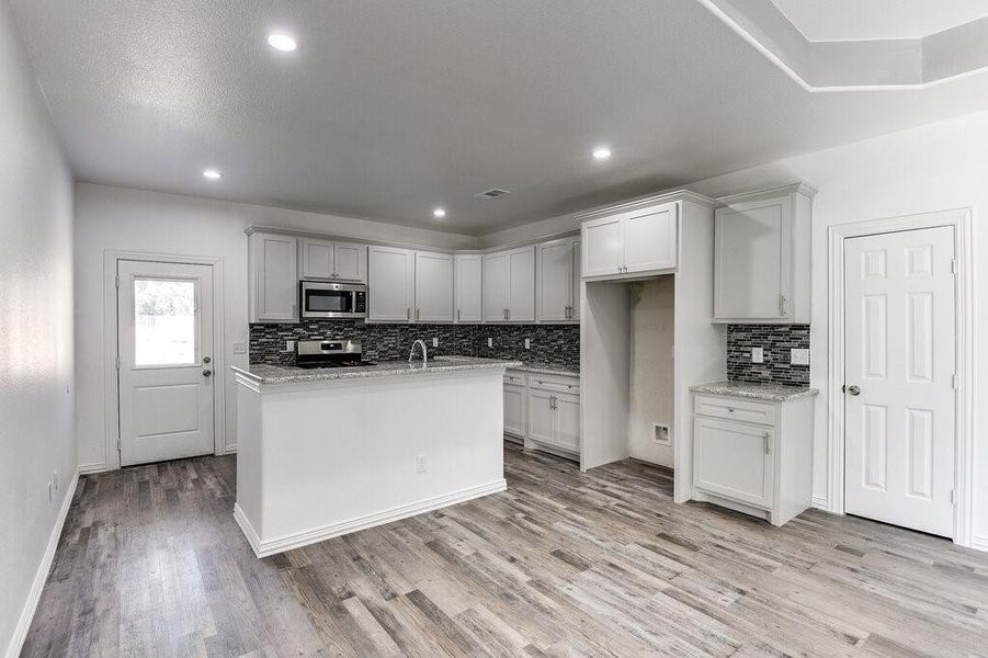 Kitchen featuring light stone countertops, appliances with stainless steel finishes, light hardwood / wood-style flooring, and a kitchen island with sink