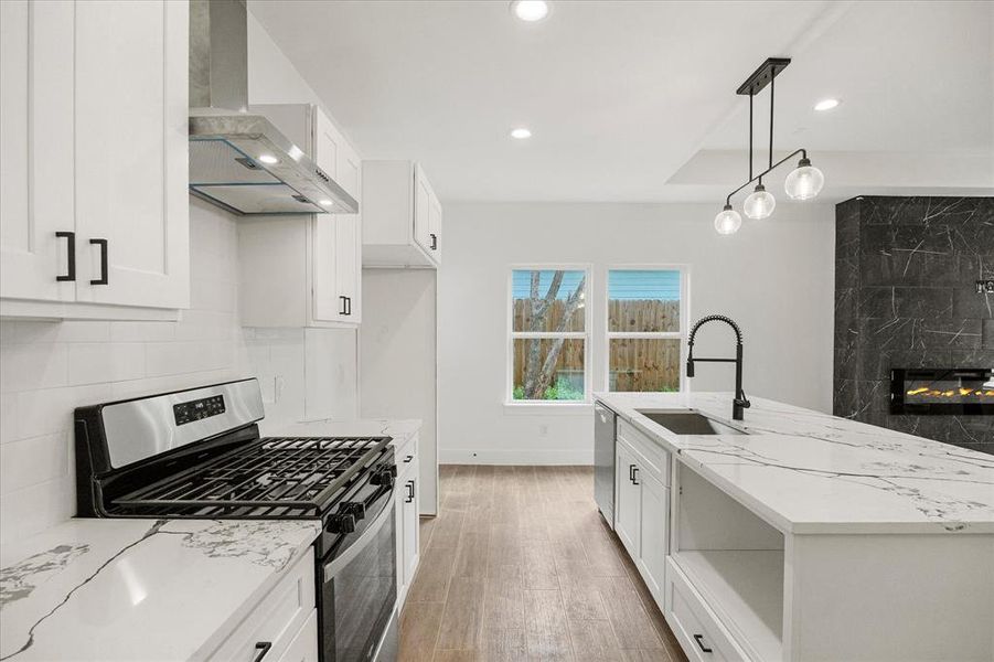 Kitchen featuring stainless steel appliances, white cabinetry, light stone counters, a kitchen island with sink, and a high end fireplace