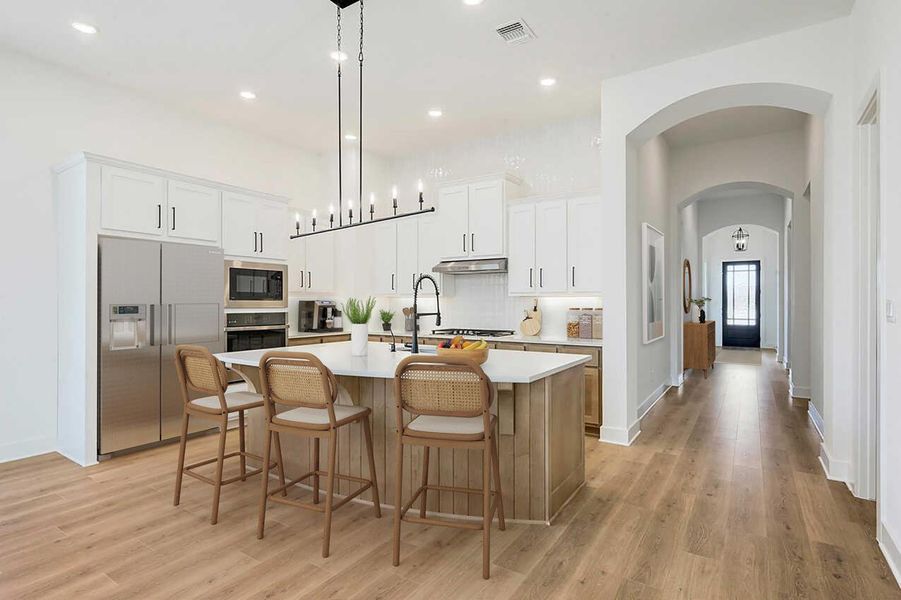 Kitchen with stainless steel appliances, light countertops, arched walkways, an island with sink, and light wood-type flooring