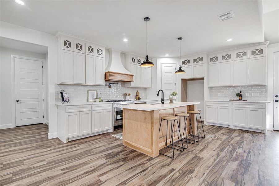 Kitchen with premium range hood, white cabinetry, high end stainless steel range, and a kitchen island with sink