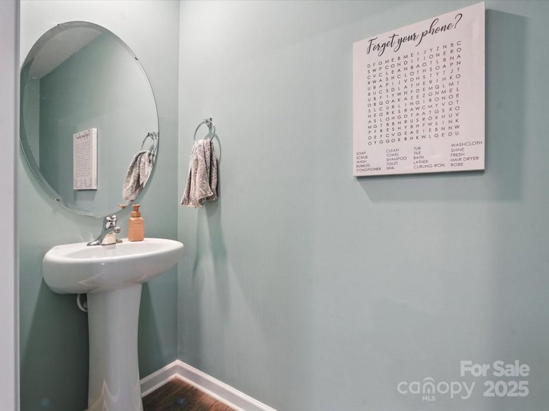 Convenient half bath featuring pedestal sink, round mirror, and decorative wall art. Neutral color palette and functional design provide perfect guest powder room on main level.