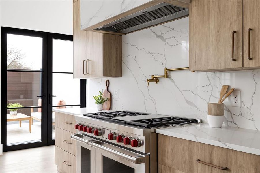 Kitchen featuring decorative backsplash, modern cabinets, light stone counters, wall chimney range hood, and double oven range