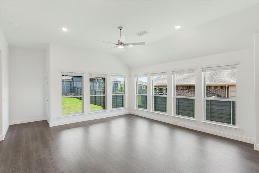 Empty living room with vaulted ceiling, ceiling fan, dark hardwood floors, and large windows overlooking backyard Empty living room with vaulted ceiling, ceiling fan, dark hardwood floors, and large windows overlooking backyard