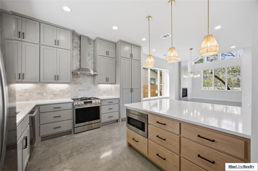 Kitchen with stainless steel appliances, backsplash, light stone counters, and gray cabinetry