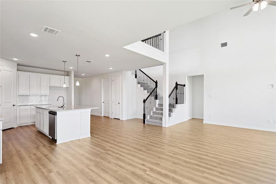 Kitchen featuring hanging light fixtures, light hardwood / wood-style floors, white cabinets, ceiling fan, and a center island with sink