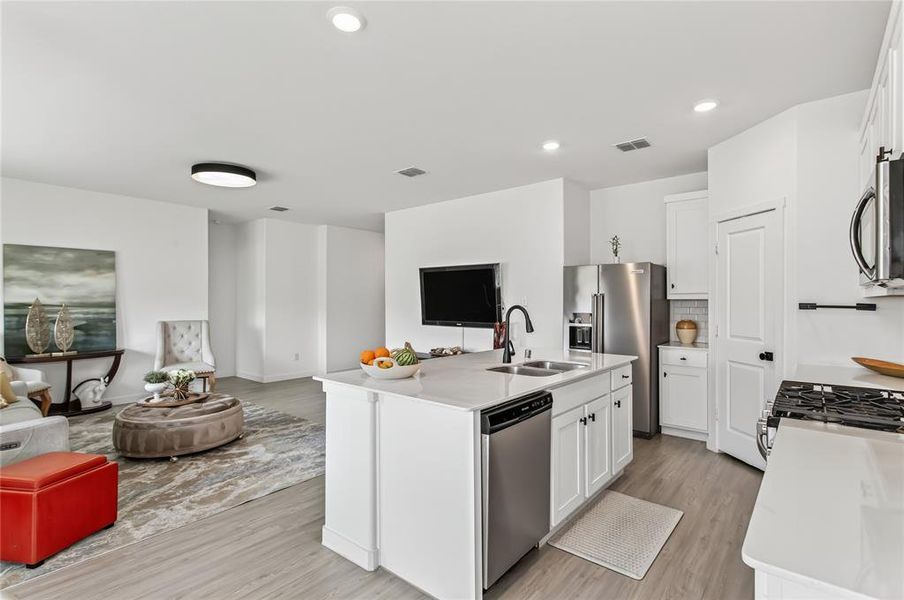 The open concept living area features light-colored flooring, a kitchen island with a sink and dishwasher, and a stainless steel refrigerator