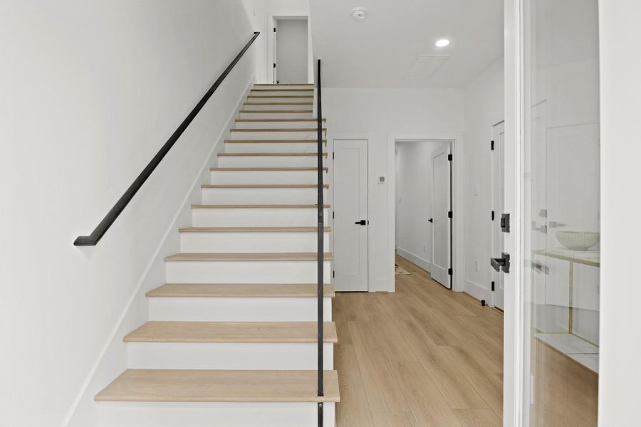 The spacious foyer of the Alexander plan includes recessed lighting, white oak luxury vinyl plank flooring, high ceilings, a nook to the right for accent furniture, entry to the first floor bedroom with ensuite bath, access to the home’s two car attached garage and a coat closet. The staircase has hardwood treads with modern wrought iron spindles leading to the second level of the home.
