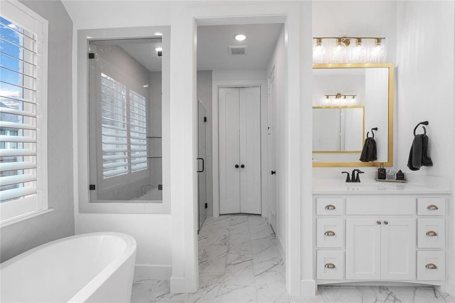 Modern bathroom featuring a freestanding soaking tub, a glass-enclosed shower, and a white vanity with a gold-framed mirror