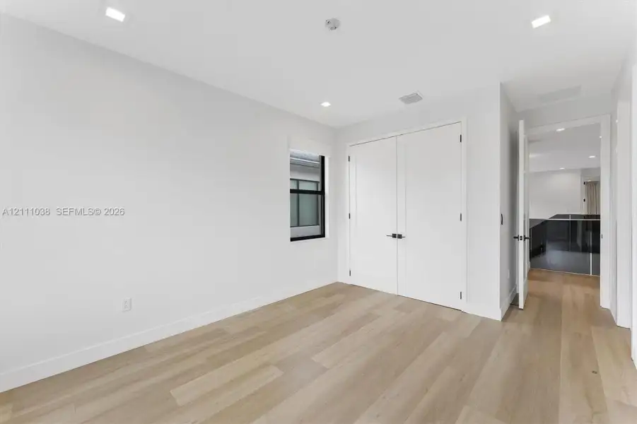 Neutral-toned interior featuring wood-finish flooring, recessed lighting, white double closet doors with matte black hardware, and a window with a black frame