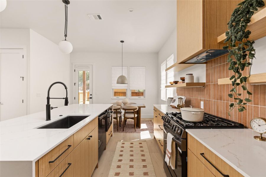 Kitchen with light stone counters, range with gas stovetop, hanging light fixtures, and healthy amount of natural light
