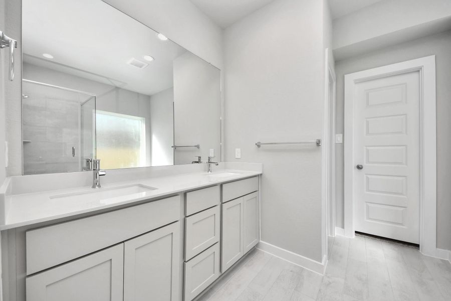 Escape to a spa-like oasis in this primary bathroom. Enjoy a walk-in shower with tile surround, a separate garden tub with custom detailing, and an elegant vanity featuring light countertops, modern hardware, and beautiful vanity lights. Experience luxury and relaxation in every detail. Sample photo of completed home with similar floor plan. Actual colors and selections may vary.