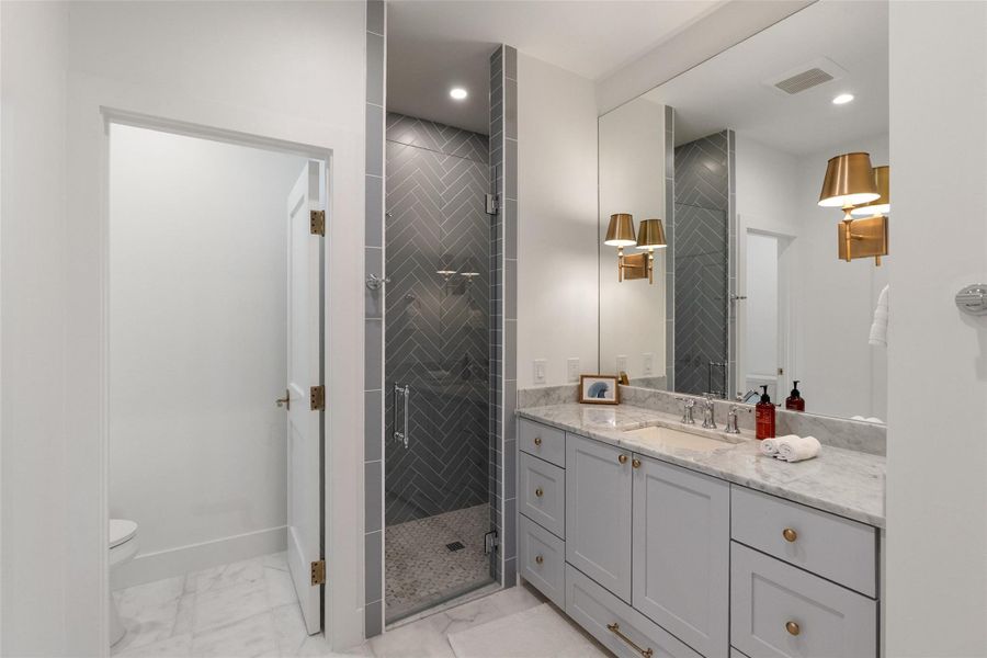 A well-appointed bathroom features a gray herringbone tile shower, a vanity with marble countertops, and a large mirror. A well-appointed bathroom features a gray herringbone tile shower, a vanity with marble countertops, and a large mirror.