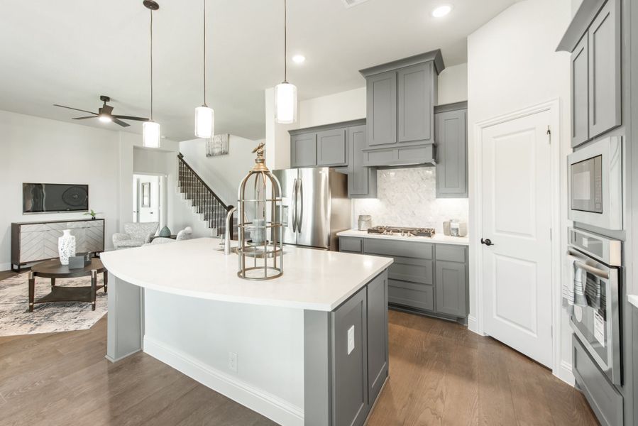Kitchen with gray cabinets, large white island, stainless steel appliances, and hardwood floors open to living area
