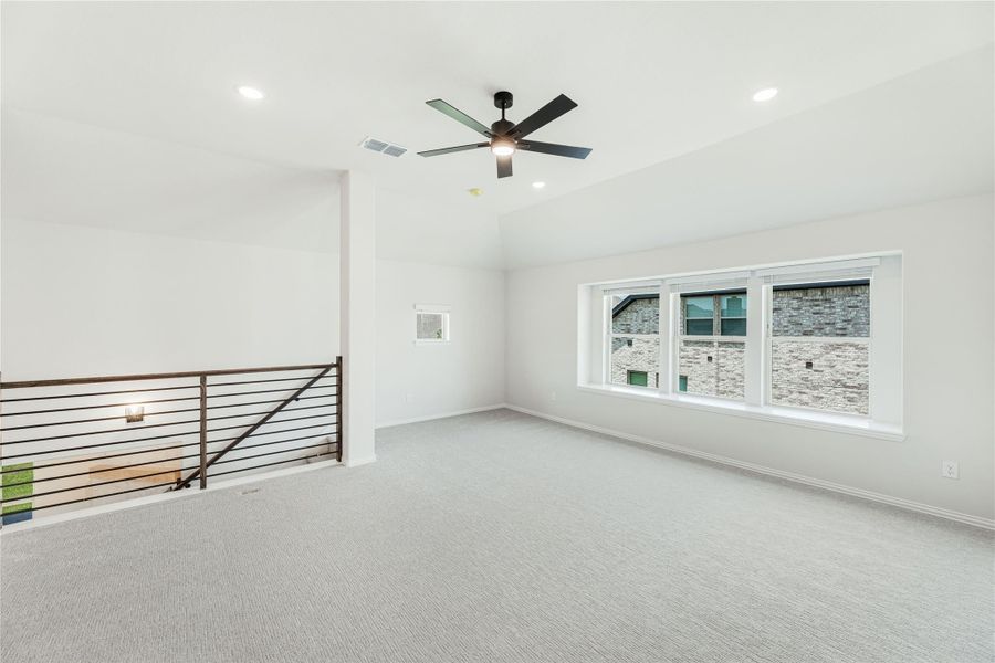Open upstairs loft with carpet, ceiling fan, large window, and metal stair railing