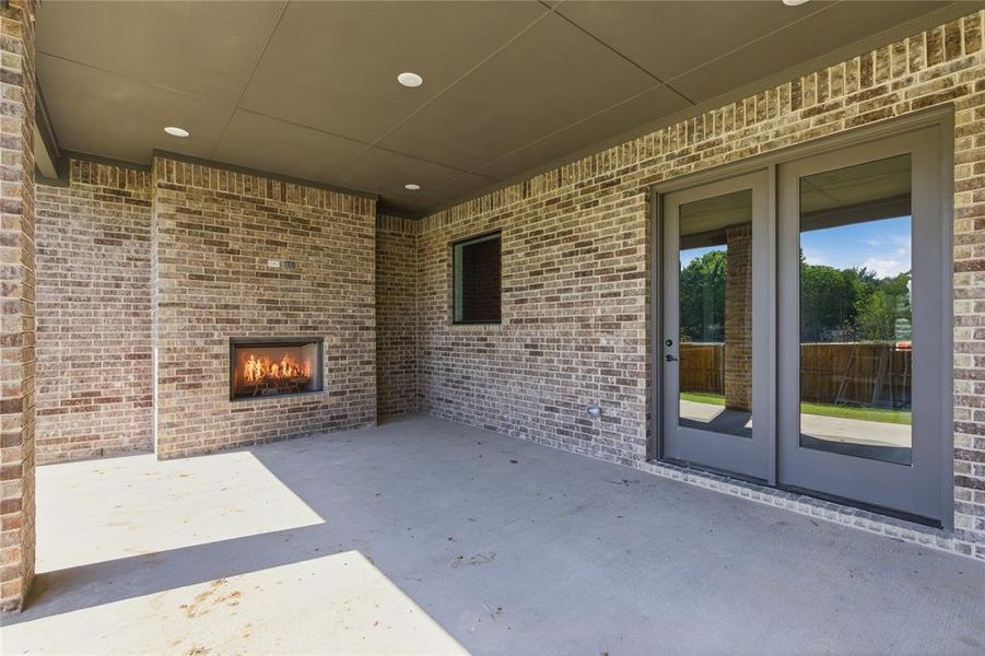 Covered outdoor patio featuring a built-in fireplace, brick construction, recessed lighting, and double glass doors