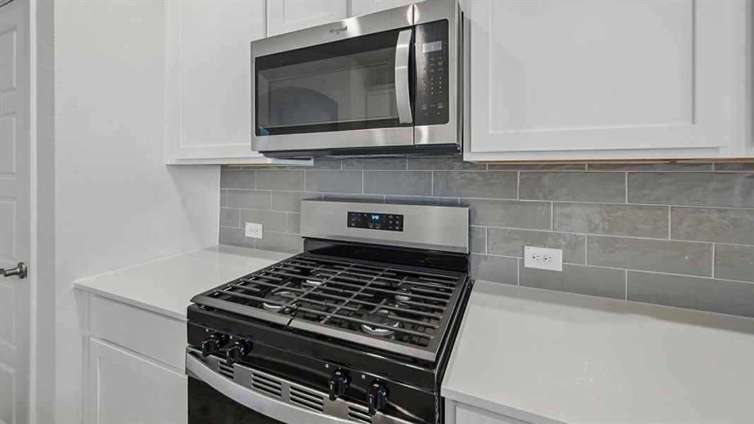 Kitchen featuring white shaker cabinetry, stainless steel microwave, stainless steel range, gray subway tile backsplash, and light-toned countertops