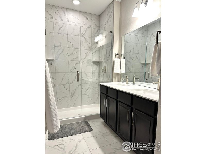 Primary bathroom features double sinks, tile floors and walk-in shower with glass shower door, large walk-in closet and additional storage space