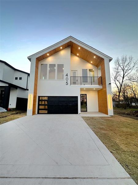 Modern home with driveway, an attached garage, a balcony, and stucco siding