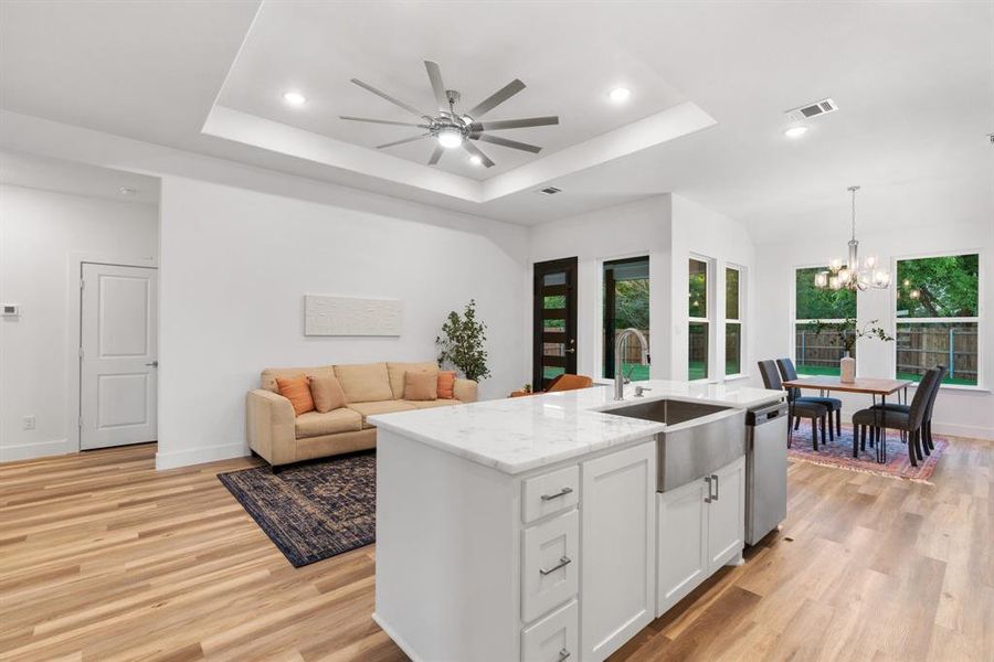 Kitchen featuring white cabinets, a raised ceiling, sink, a center island with sink, and light hardwood / wood-style flooring