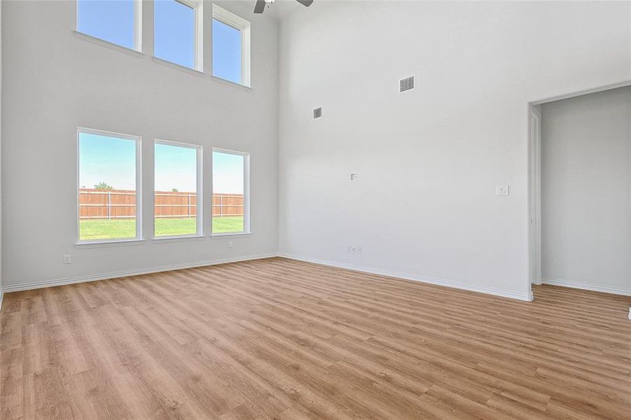 Unfurnished living room with ceiling fan, light wood-type flooring, and a towering ceiling