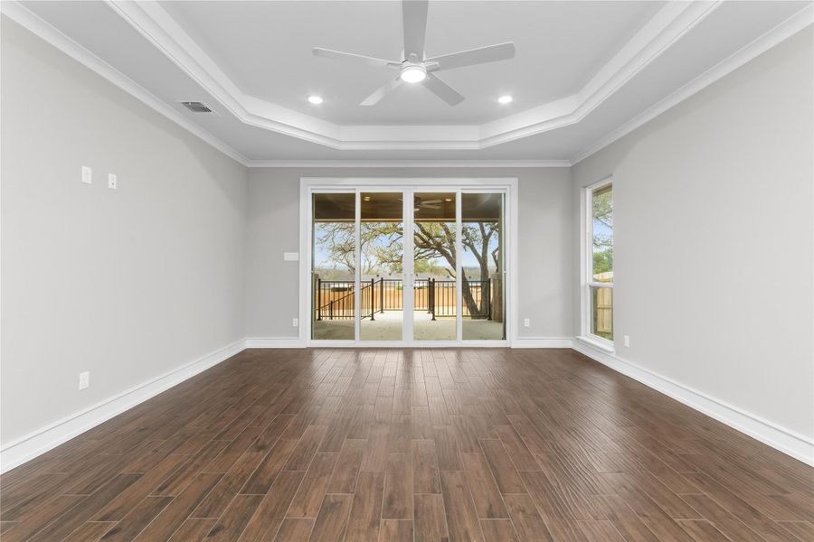 Spare room featuring a tray ceiling, a ceiling fan, dark wood-style flooring, ornamental molding, and baseboards Spare room featuring a tray ceiling, a ceiling fan, dark wood-style flooring, ornamental molding, and baseboards
