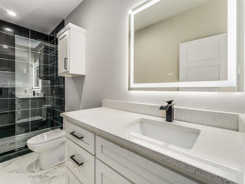 Bathroom featuring a tile shower, vanity, and toilet