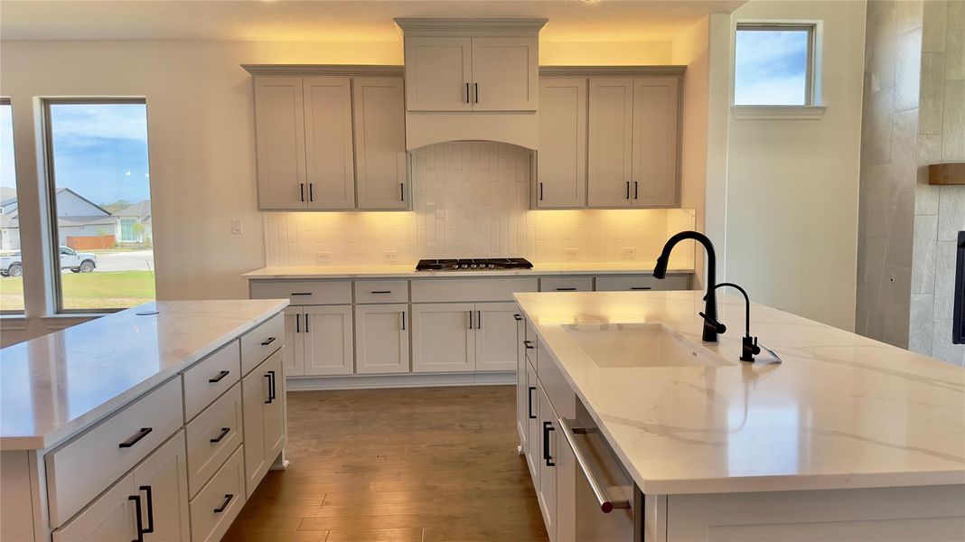 Kitchen with a kitchen island with sink, light stone countertops, dark wood-type flooring, backsplash, and stainless steel appliances