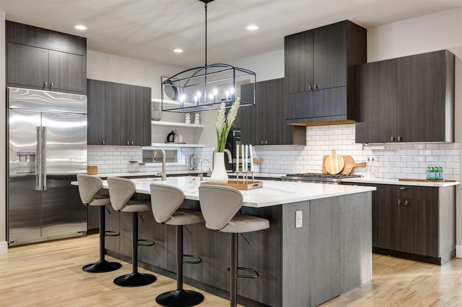 Kitchen with a center island with sink, stainless steel built in fridge, pendant lighting, and light hardwood / wood-style flooring