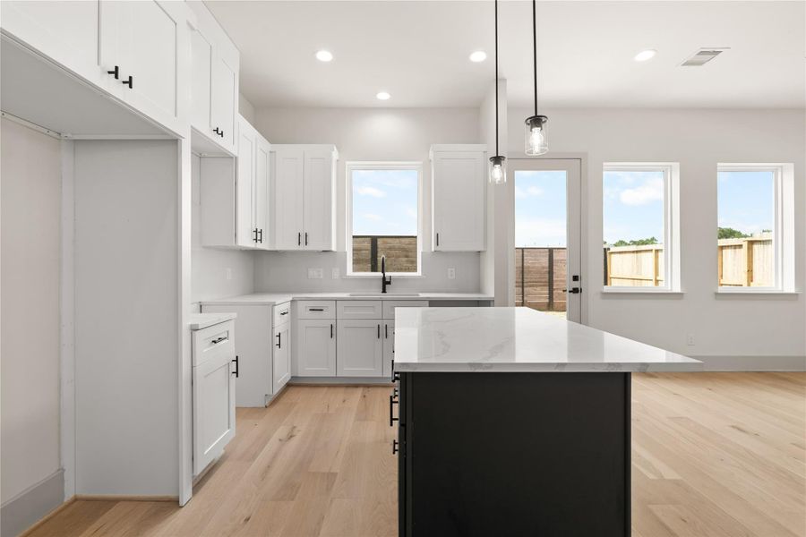 Kitchen with white shaker cabinetry, dark island, and quartz countertops Kitchen with white shaker cabinetry, dark island, and quartz countertops