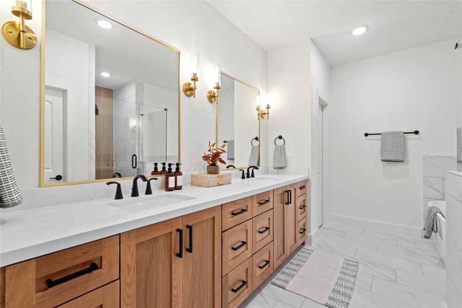 Luxurious primary bathroom featuring a double vanity with quartz countertops, modern matte black fixtures, and elegant gold-accented mirrors - combining warmth and sophistication in one space.