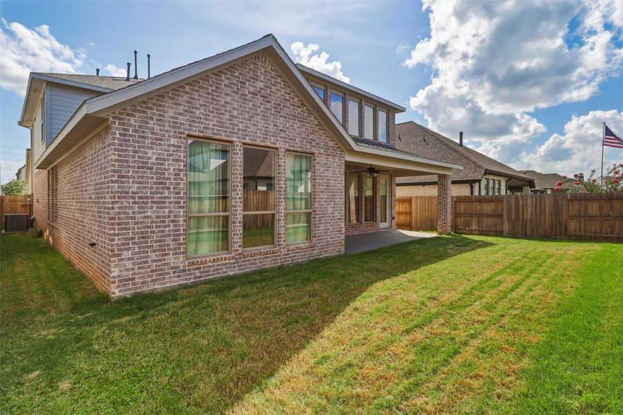 This rear exterior view highlights the home's attractive design, featuring a large covered patio, expansive windows, and a generously sized backyard with plenty of room to personalize your outdoor living space.