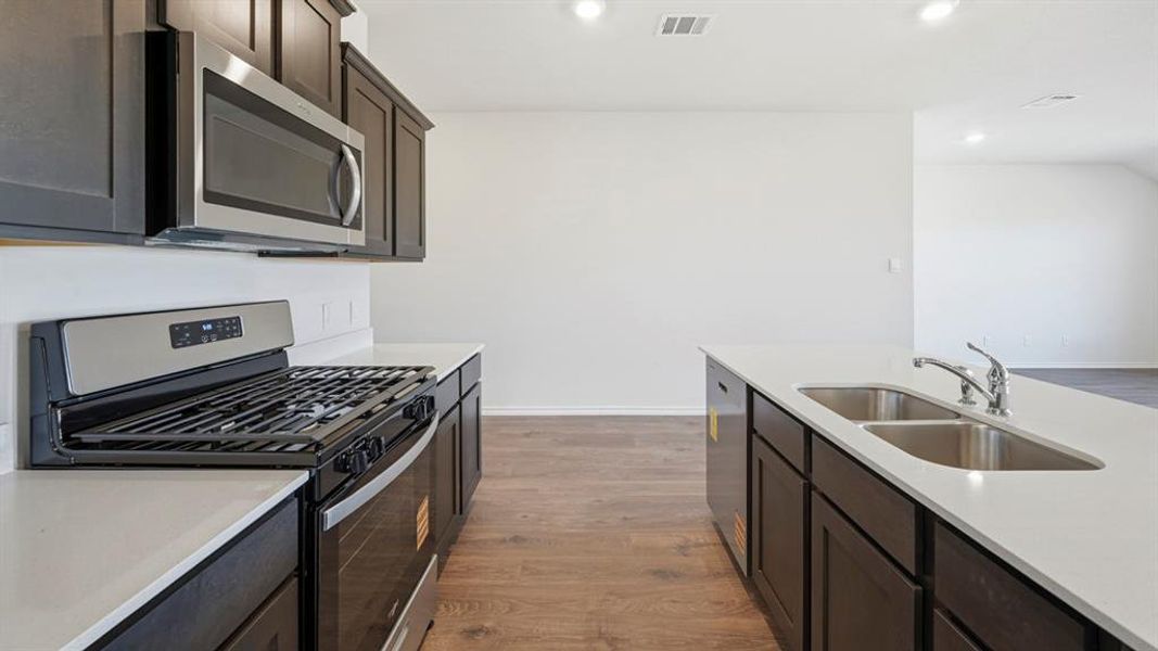 Kitchen featuring stainless steel appliances, dark brown cabinetry, light wood-type flooring, light stone counters, and recessed lighting