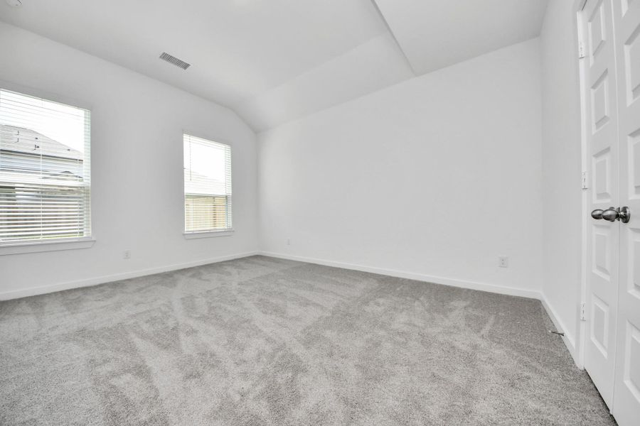 Escape and relax in the exquisite primary suite, a haven to unwind after a long day. The spacious room, located on first floor, boasts plush carpeting, soothing paint tones, high ceilings, and expansive windows adorned with privacy blinds. Sample photo of completed home with similar floor plan. Actual colors and selections may vary.