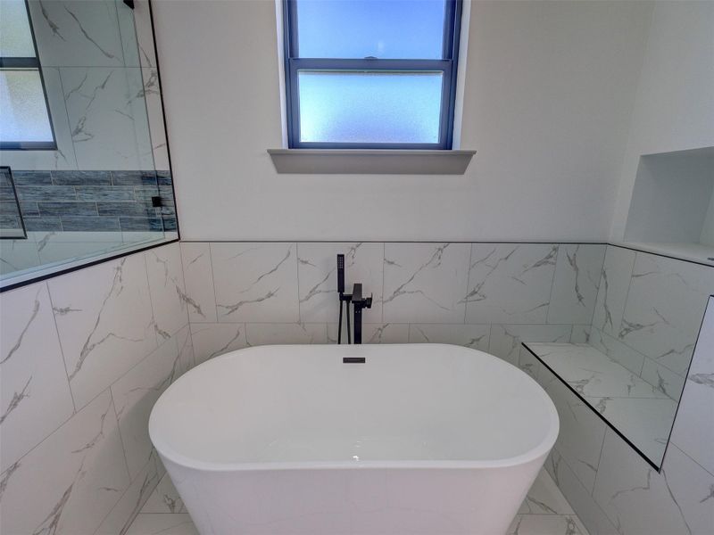 Crisp marble-patterned tile surrounds a modern freestanding soaking tub beneath a frosted privacy window.