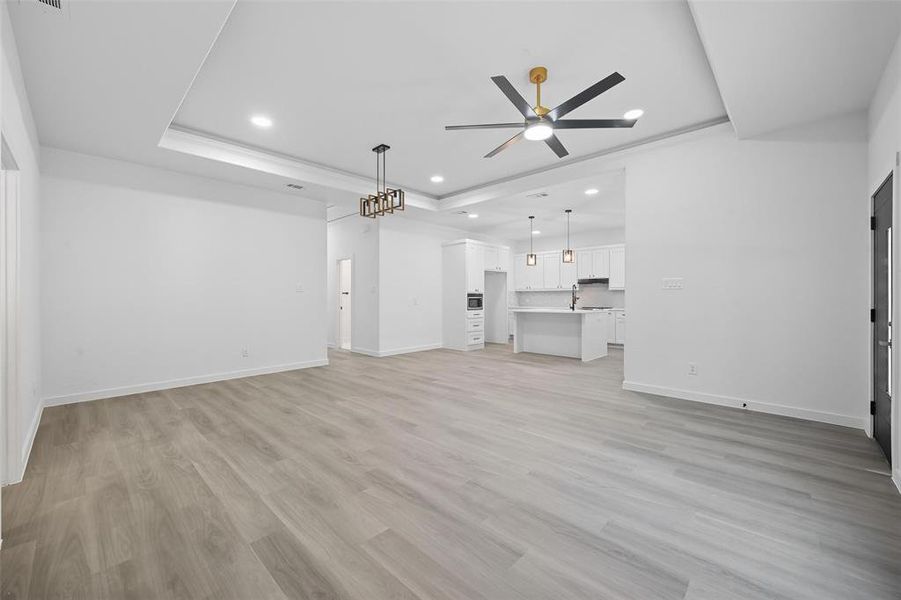 Unfurnished living room featuring a tray ceiling, light wood-type flooring, recessed lighting, and ceiling fan Unfurnished living room featuring a tray ceiling, light wood-type flooring, recessed lighting, and ceiling fan