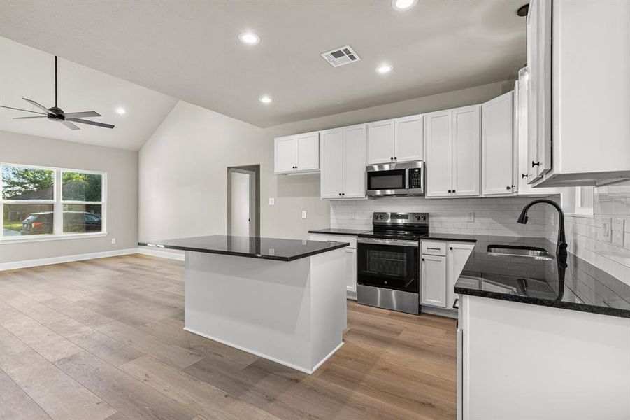 Kitchen with tasteful backsplash, lofted ceiling, stainless steel appliances, a center island, and white cabinets Kitchen with tasteful backsplash, lofted ceiling, stainless steel appliances, a center island, and white cabinets