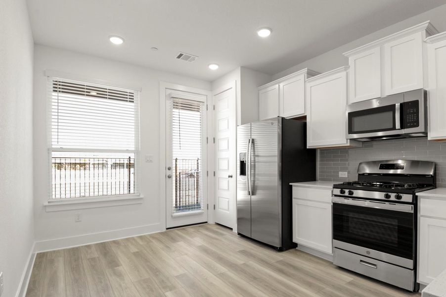 Kitchen featuring appliances with stainless steel finishes, white cabinetry, light wood finished floors, backsplash, and recessed lighting