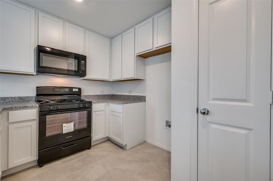 Kitchen featuring black appliances, white cabinets, and light tile floors Kitchen featuring black appliances, white cabinets, and light tile floors