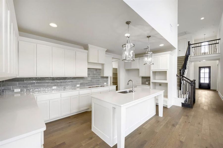 Contemporary kitchen featuring white cabinetry, light-toned countertops, a full-height gray tile backsplash, and wood-finish flooring Contemporary kitchen featuring white cabinetry, light-toned countertops, a full-height gray tile backsplash, and wood-finish flooring