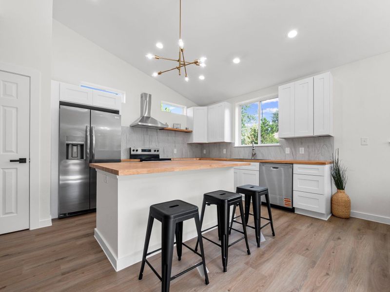 Bright kitchen featuring a central island, wood-finish countertops, stainless steel appliances, white cabinetry, and wood-finish flooring
