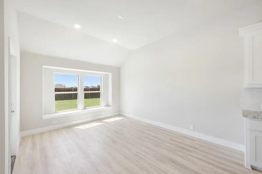 Empty room with vaulted ceiling, light wood floors, and double window overlooking backyard