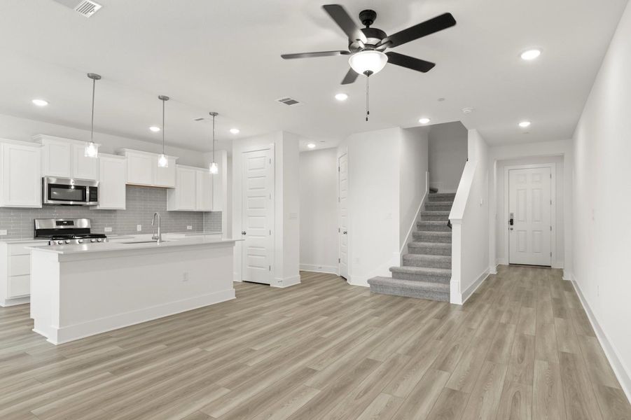 Kitchen featuring pendant lighting, white cabinets, an island with sink, open floor plan, and stainless steel appliances