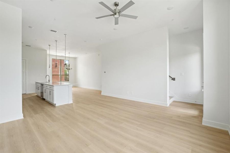 Unfurnished living room featuring a sink, ceiling fan, light wood finished floors, and baseboards