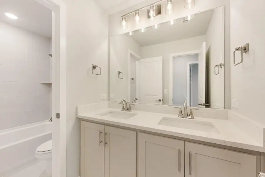 Bathroom with double sink vanity, gray cabinets, quartz countertop, and tub-shower combo with white tile