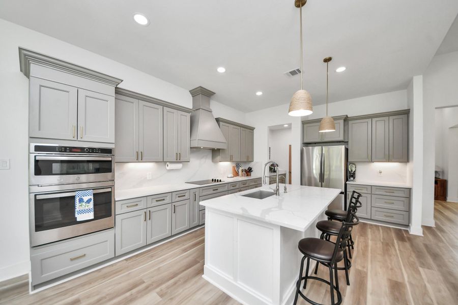 Spacious modern kitchen featuring elegant gray cabinetry, a large island with the option for seating, stainless steel appliances, and sleek pendant lighting. Spacious modern kitchen featuring elegant gray cabinetry, a large island with the option for seating, stainless steel appliances, and sleek pendant lighting.
