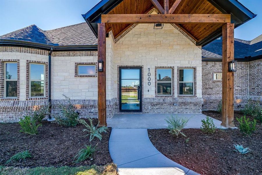 Entrance to property featuring a shingled roof, covered porch, and stone siding